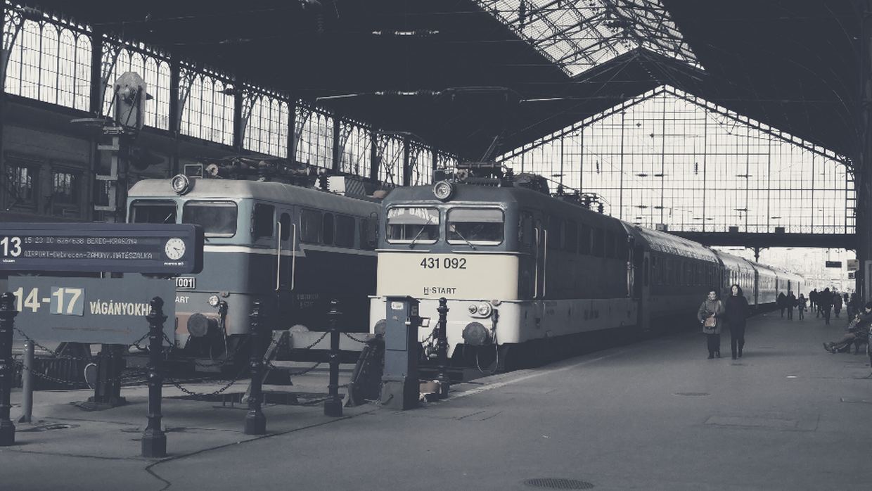 Deux locomotives à l'arrêt sous la verrière d'une grande gare d'Europe centrale, quais presque vides.
